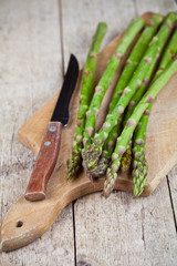 Canvas Print - Fresh raw garden asparagus and knife closeup on cutting board on rustic wooden table background. Green spring vegetables.