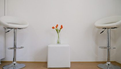 Two White chairs and orange tulips on the table in a saloon