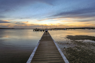 Wall Mural - Timber jetty leading to sun setting over ocean