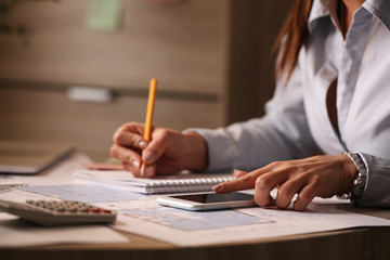 Close up of businesswoman using phone while taking notes in the office.