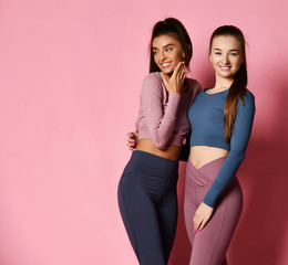 two sport girls international friends in modern high-tech colorful sportswear posing on pink