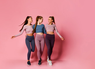three pretty athletic girls in high-tech modern colorful sportswear vigorously walk together towards
