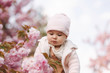 © Aleksandr - Cute baby girl between pink branches play with leaflets. Happy little girl surrounded by sakura