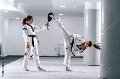 Plakaty Taekwondo  piekny-kaukaski-dziewczyna-sportowy-w-dobok-kopiac-podczas-gdy-drugi-trzyma-cel-kopniecia