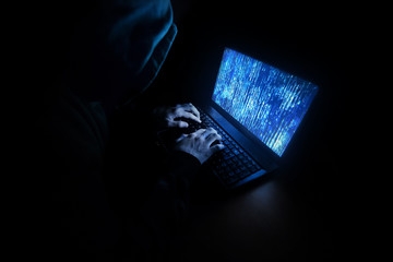 Young male hacker in hoodie working on laptop. Cybercrime - internet security concept