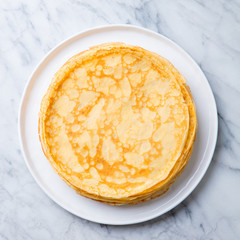 Wall Mural - Crepes, thin pancakes on a white plate. Marble background. Copy cpace. Top view.