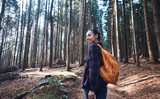 Fototapeta Las - Portrait of a woman hiker walking on the trail in the woods. Beautiful happy stylish traveling girl with backpack on a forest background.