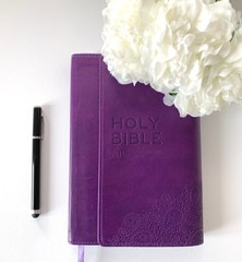 Wall Mural - Baselland, Switzerland - 03.05.2019. Bible flat lay on a white Table with different accessories; white flowers, black pen, purple Holy Bible, etc. 