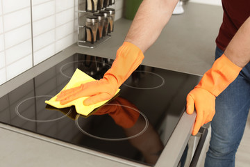 Sticker - Young man cleaning oven cooktop with rag in kitchen, closeup