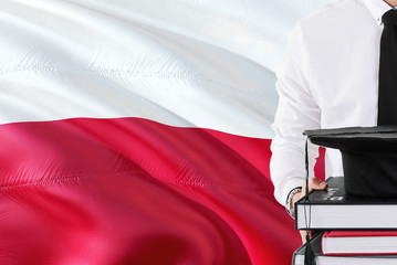 Successful Polish student education concept. Holding books and graduation cap over Poland flag background.