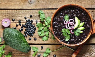 Sticker - thick black bean soup or stew. Latin American or Mexican cuisine. stewed black beans served with avocado and red onion and cilantro. place for text. top view.