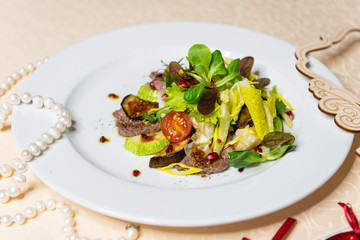 Salad from beef and fresh vegetables on a white plate in the interiors of the restaurant.