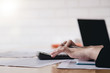 © Natee Meepian - Business woman using calculator and laptop for do math finance on wooden desk in office and business working background, tax, accounting, statistics and analytic research concept
