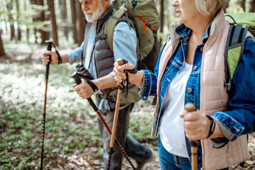 Wall Mural - Senior man and woman hiking with trekking sticks in the forest, close-up view with cropped face