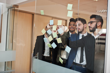 Wall Mural - Business mans pointing on glass with colorful paper notes. Diverse group of male employees in formal wear using stickers.