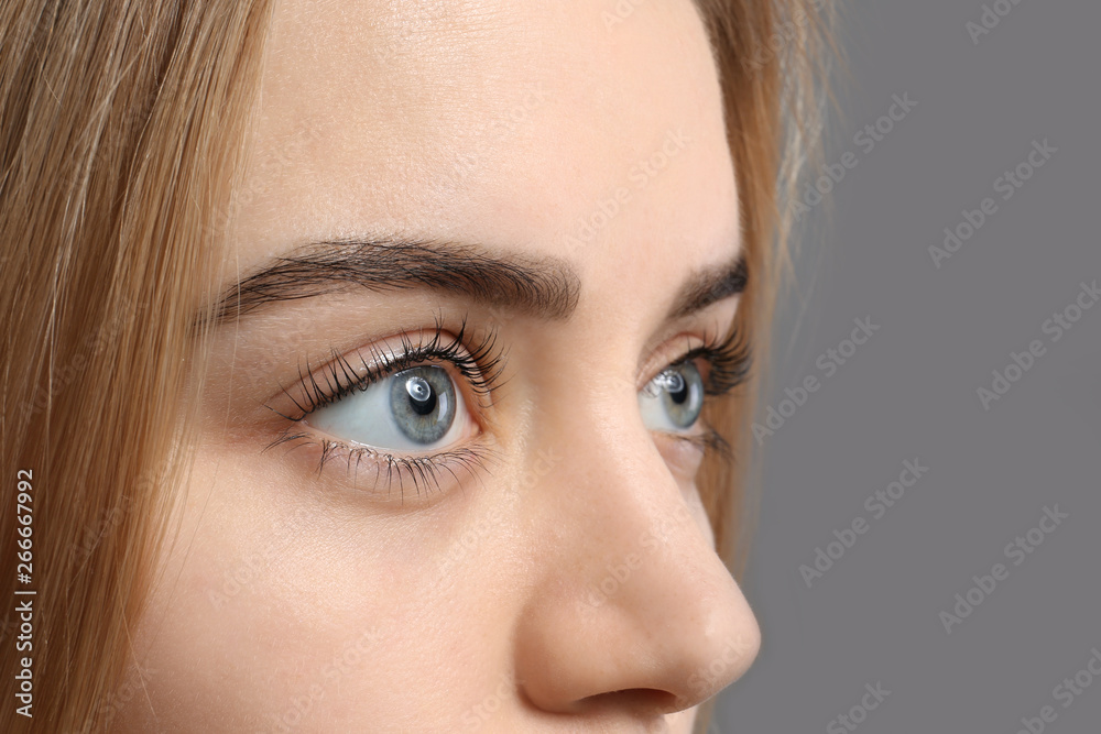 Beautiful young woman with laminated eyelashes on grey background, closeup