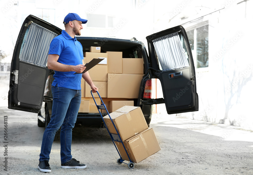 Handsome delivery man near car with parcels outdoors