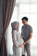 asian muslim pregnant woman with her husband hold on tummy at home