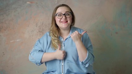 Wall Mural - Portrait of attractive plus size  in glasses woman having emotions positive, joy and surprise isolated over colored background. Concept of emotions. Raised up thumb.