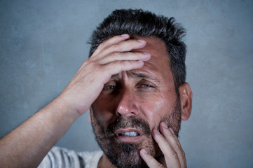 Wall Mural - close up dramatic  portrait of young attractive anxious and depressed man in pain with hands on his head suffering headache and migraine and depression crisis