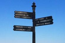 Black Iron Signpost Giving Directions To The Thames Path, Rotherhithe, Surrey Docks Farm, Greenland Dock Walk, Greenland Lock, Foot Tunnel, Thames Path, And Deptford Wharf In East London.