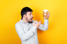 Studio Portrait Of A Surprised Man Who Is Outraged By The Quality Of Beer, Over Yellow Background