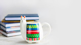 Fototapeta Młodzieżowe - White Llama mug with pile of books on light grey empty background, horizontal with copy space for text or design. Trendy animal accessories for school, office