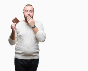 Sticker - Young hipster man eating chocolate bar over isolated background cover mouth with hand shocked with shame for mistake, expression of fear, scared in silence, secret concept