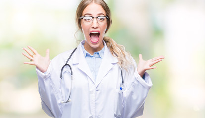 Poster - Beautiful young blonde doctor woman wearing medical uniform over isolated background celebrating crazy and amazed for success with arms raised and open eyes screaming excited. Winner concept