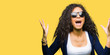 Young beautiful girl with curly hair wearing fashion sunglasses crazy and mad shouting and yelling with aggressive expression and arms raised. Frustration concept.
