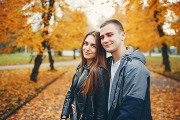 Cute couple walking in a autumn park. Boy in a black jacket. Girl in a gray dress