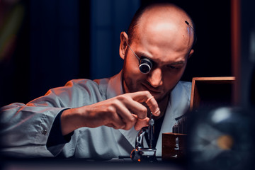 Wall Mural - Focused man is working at his workshop with monocle and other tools repairing old watches.