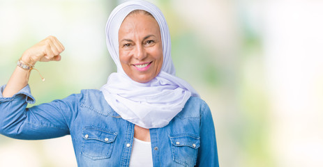 Middle age eastern arab woman wearing arabian hijab over isolated background Strong person showing arm muscle, confident and proud of power