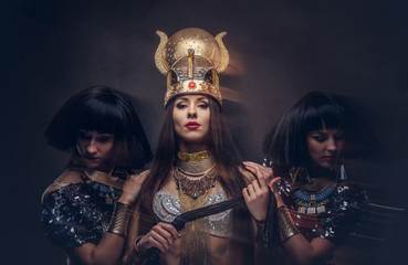 Portrait of haughty Egyptian queen in an ancient pharaoh costume with two concubines. Isolated on a dark background.