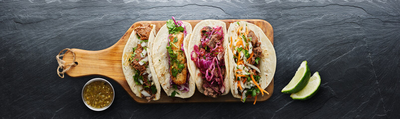 four mexican street tacos with fish barbacoa and carnitas shot in panoramic composition on top of se