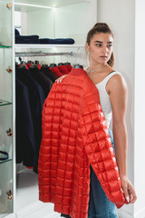 Young woman in a blu jeance white t-shirt trying on red down coat in a luxury boutique