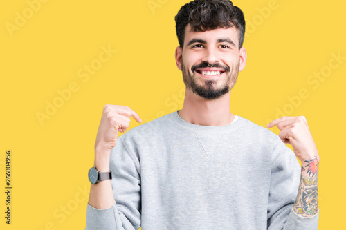 Cuadros en Lienzo Young handsome man wearing sweatshirt over isolated background looking confident with smile on face, pointing oneself with fingers proud and happy