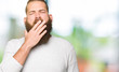 © Krakenimages.com - Young blond man wearing casual sweater bored yawning tired covering mouth with hand. Restless and sleepiness.