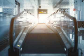 Wall Mural - A long modern travelator indoors of an airport terminal with bright exit in front; glass corridor with a contemporary moving walkway in interior of departure or arrival area railway station depot