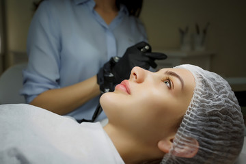 Wall Mural - Permanent make up eyeliner procedure, applying on young girl. Close-up. Young beautiful woman making permanent makeup in cosmetology salon. Young girl applying permanent eyeliner in beauty studio