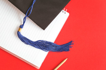 Wall Mural - Black Graduation Cap with notebook on red background. Masters or Bachelors Degree thesis writing. Knowledge qualifications and higher education with copy space