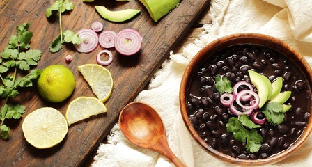 Sticker - thick black bean soup or stew. Latin American or Mexican cuisine. stewed black beans served with avocado and red onion and cilantro. place for text. top view.