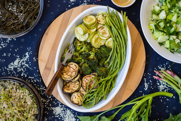 Baked roasted seasonal vegetables for vegan lunch or vegetarian dinner on table with mustard, spinach and fresh salad.