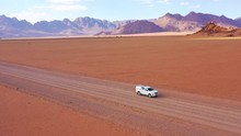 High Aerial Over A Toyota Safari Vehicle Heading Across The Flat, Barren Namib Desert In Namibia.