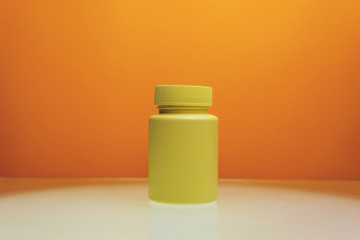 Poster - Yellow bottle for pills on a white table and orange background.