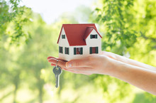 Mortgage, Real Estate And Property Concept - Close Up Of Hands Holding House Model And Home Keys Over Green Natural Background