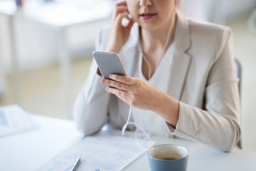 business, technology and music concept - smiling businesswoman with earphones and smartphone at office