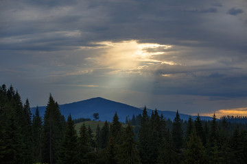 Wall Mural - Sun shines through the gap in overcast dramatic sky over mountains