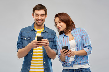 technology and people concept - happy couple using smartphones over grey background