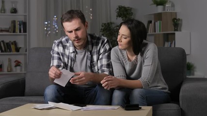 Wall Mural - Angry couple waiting after calling on phone to claim a wrong bank receipt in the night at home